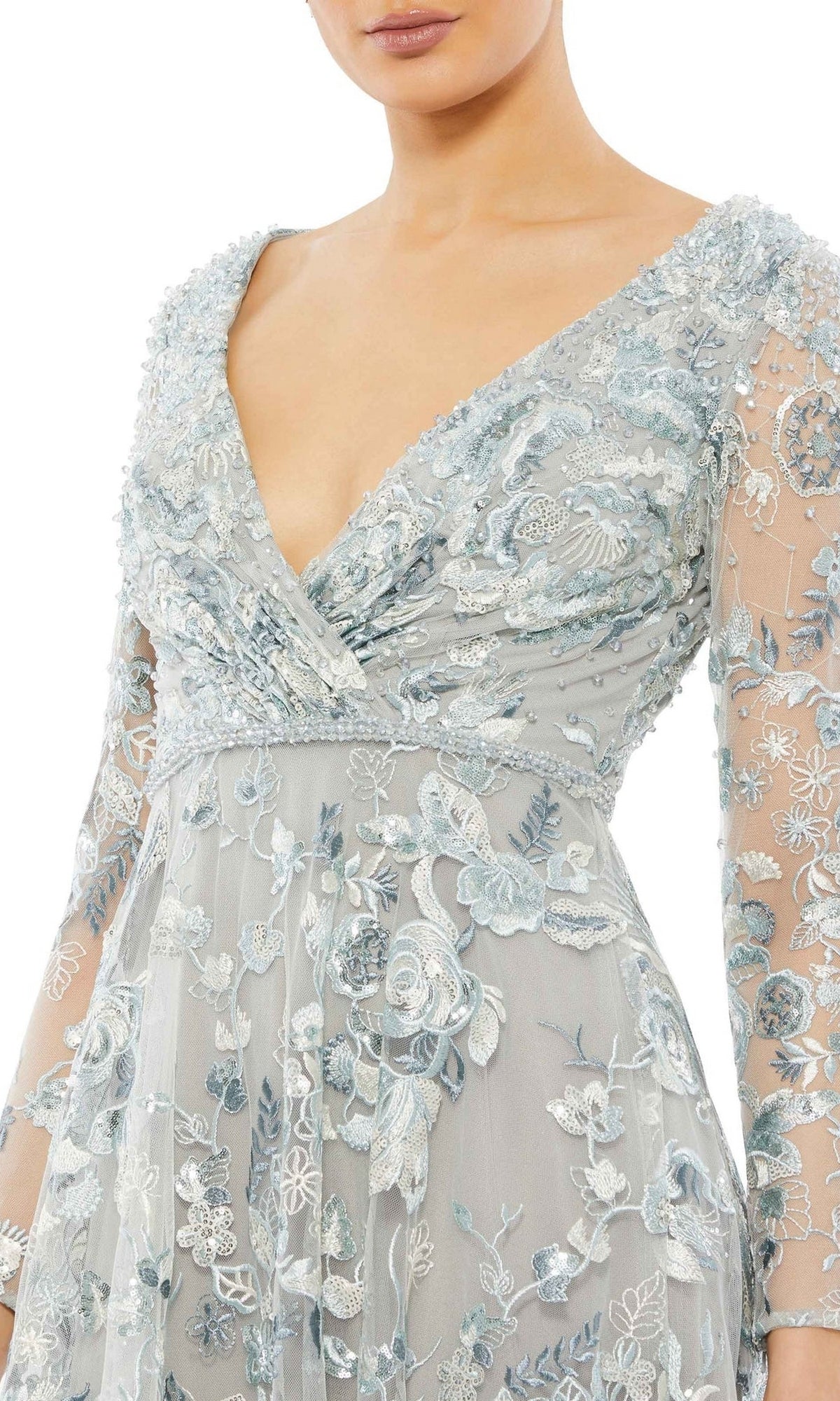 A person wearing the Mac Duggal 67869 Long Sleeve Lace Formal Dress in light blue, featuring intricate floral embroidery and a deep V-neckline.